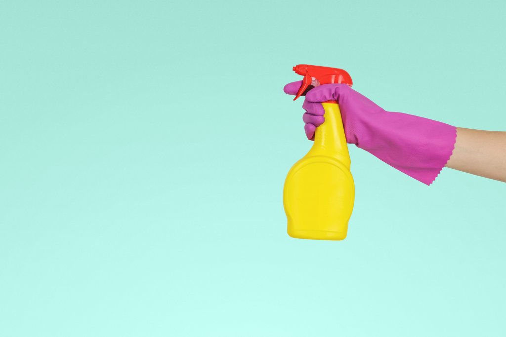 yellow spray bottle being held by arm with pink glove. ingredients to avoid, clean up your cleaning products: a guide