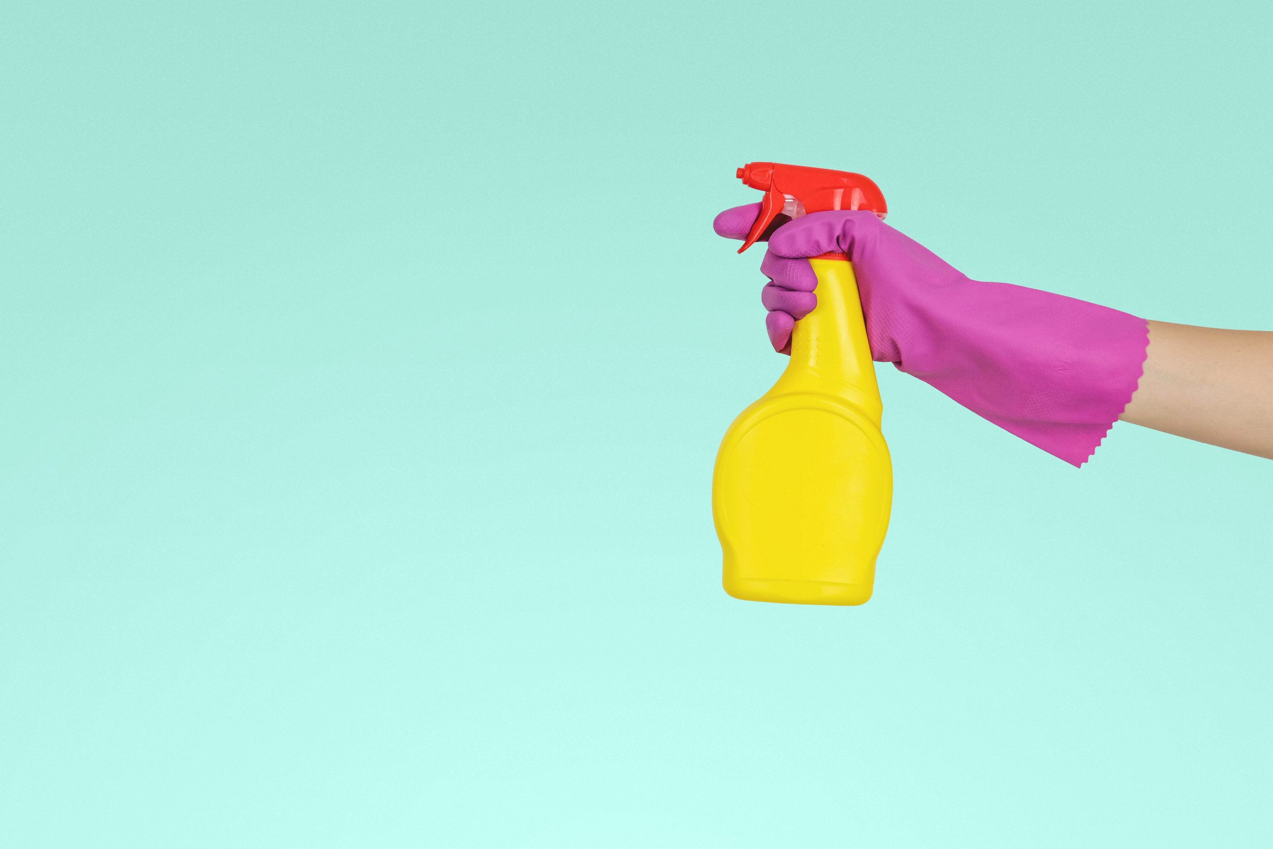 cleaner's hand with a rubber glove holding a cleaning solution spray bottle