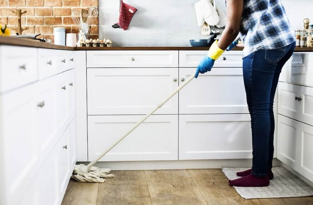 man wearing cleaning gloves while mopping a kitchen floor
