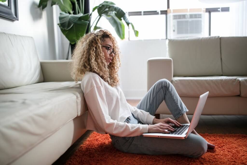 woman sitting on floor in front of couch using laptop