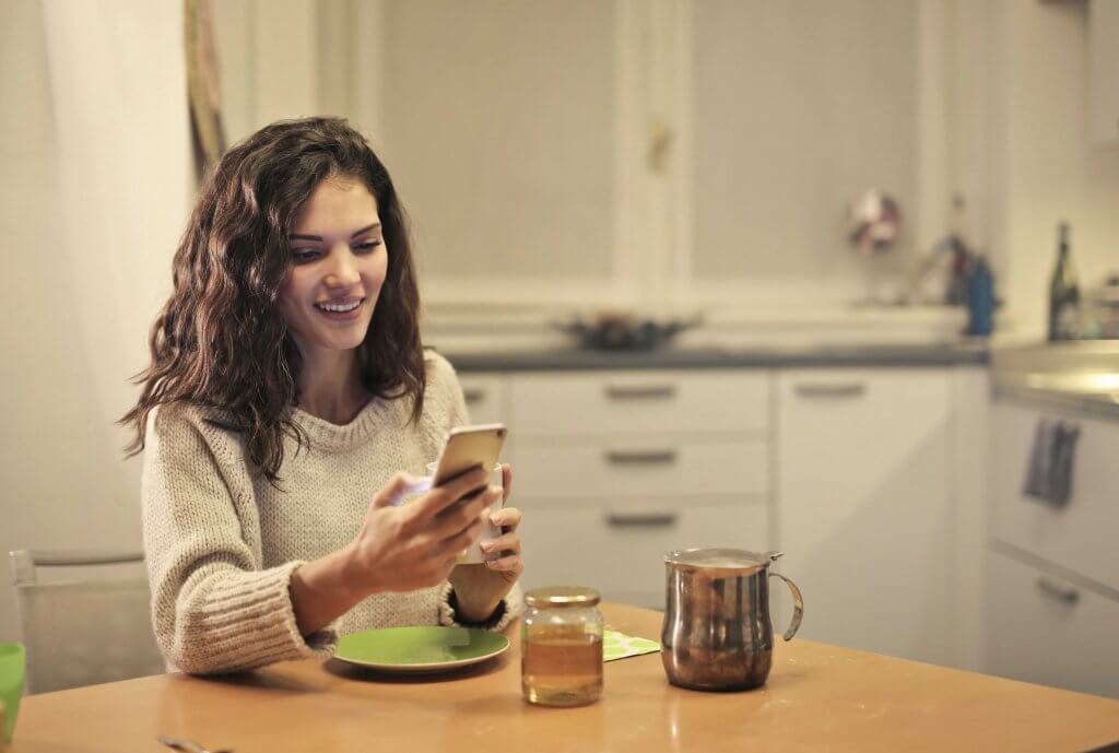 young woman sitting at a kitchen table looking at her smartphone