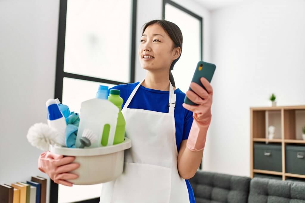 professional cleaner holding a container of cleaning supplies and her smartphone in the other hand